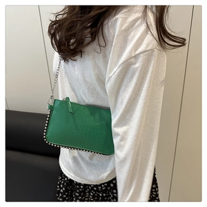 Green crocodile texture shoulder bag with silver studs and chain strap on a model