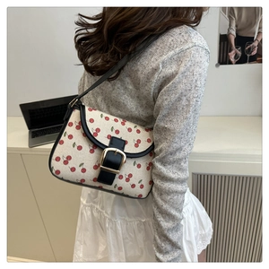 Close-up of cherry print canvas shoulder bag with black leather flap and gold buckle detail