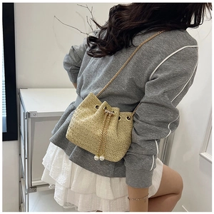 Detail view of woven straw bucket bag with golden chain strap and pearl drawstring tassels
