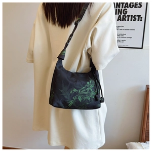 Close-up of black nylon crossbody bag with green leaf print worn by model from behind