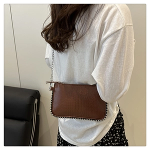 Detail of a brown crocodile-patterned chain bag with elegant silver beaded trim accents