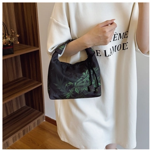 Detail of the green leaf pattern on a black crescent handbag with a drawstring zipper