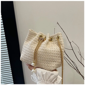 Detailed shot of woven bucket bag featuring gold chain drawstring and white pearl charms