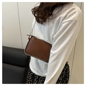 Detailed view of brown crocodile texture and silver bead trim on a chain crossbody bag