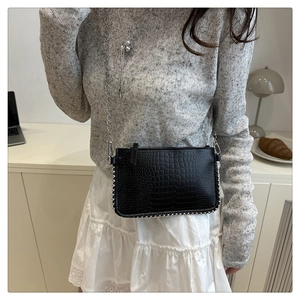 Detail of black faux crocodile leather crossbody bag with silver bead trim and chain strap