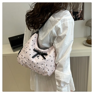 Détail du sac épaule matelassé rose avec nœuds noirs et breloque porté par un mannequin