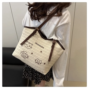 Detailed close-up of a woven tote bag with cat embroidery and brown leather straps