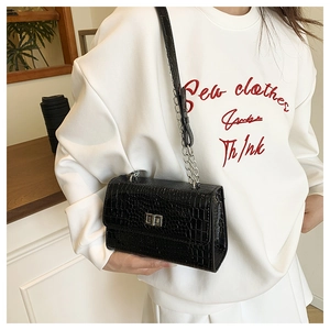 Detail of glossy crocodile-patterned bag with silver square twist lock and chain strap