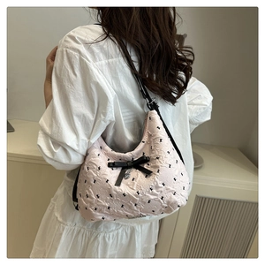 Détail du sac rose texturé avec nœuds noirs et pendentif cœur argenté sur la bandoulière