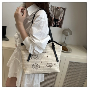 Detail of woven straw tote bag with cartoon cat embroidery and black shoulder straps