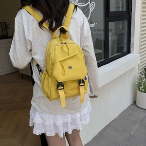 Bright yellow minimalist backpack with adjustable straps shown in a casual outdoor setting