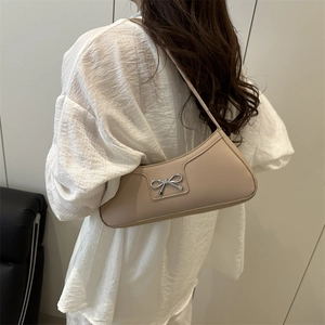 Chic beige crescent hobo bag with silver bow detail worn by woman in white shirt