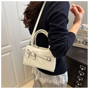 Detail of a creamy white crossbody bag with bow decoration shown on a model