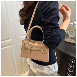 Detail of beige shoulder bag with bow decor shown on model in modern home interior