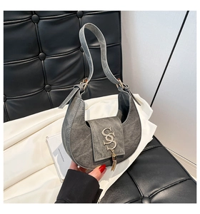 Detail of grey denim crescent bag showing gold SS logo and elegant long fringe tassel