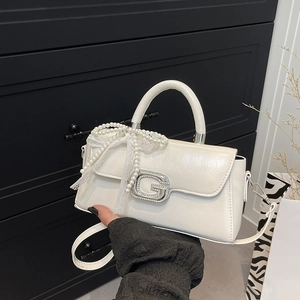 Detail of white glossy leather square bag featuring a crystal G buckle and pearl lace bow