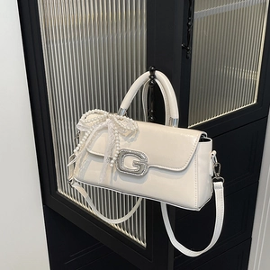 Detail of white leather bag with rhinestone G buckle and pearl bow charm on vintage cabinet