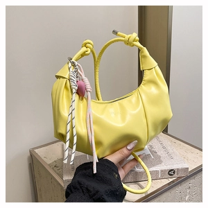 Close-up of bright yellow pleated hobo bag with colorful woven charms and zipper detail