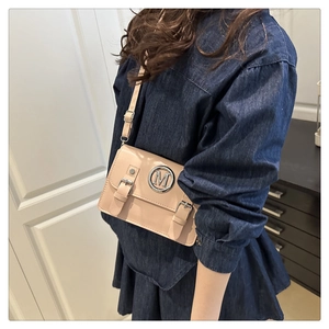 Detail of minimalist beige crossbody bag featuring a round metal M logo and strap accents