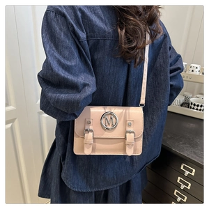 Detail of a pink square crossbody bag featuring a round metal M-logo and double buckle straps
