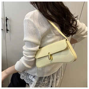 Detail of a creamy baguette shoulder bag with a gold twist-lock on a fashion model
