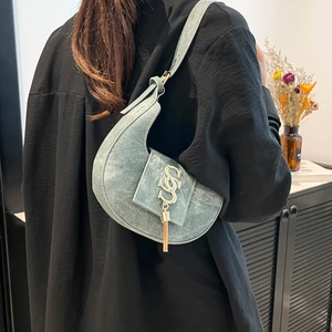 Blue denim crescent bag with gold logo and tassels worn as an elegant shoulder bag