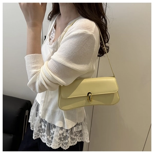 Detail of light yellow PU leather underarm bag featuring a gold metal lock and slim strap