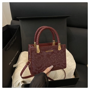 Detail der burgunderroten Handtasche mit Schlangenmuster, Flechtgriff und goldener Hardware