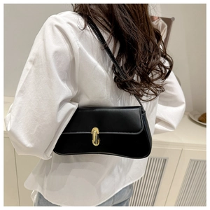 Close-up of minimalist black baguette bag with gold twist lock on shoulder of a model