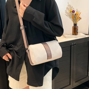 White cylinder pillow bag with ethnic woven strap shown on a model in a modern room
