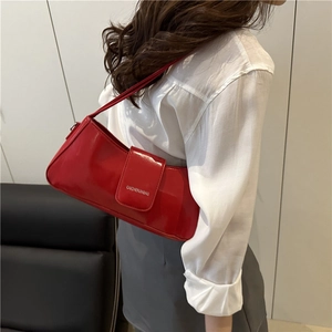 Glossy red patent leather baguette shoulder bag shown on model in a modern interior