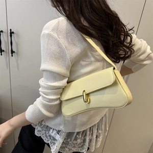 Minimalist pale yellow baguette shoulder bag with gold metal clasp on a female model