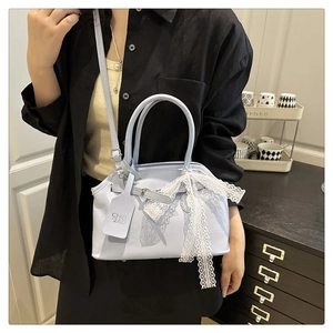 Detail view of light blue leather square bag with white lace bow and adjustable strap