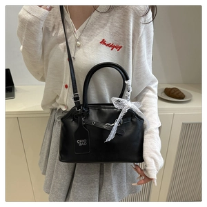 Détail du sac en cuir noir avec nœud en dentelle blanche et étiquette de marque