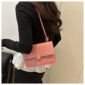 Pink crossbody square bag with crocodile pattern and knotted strap detail worn by model