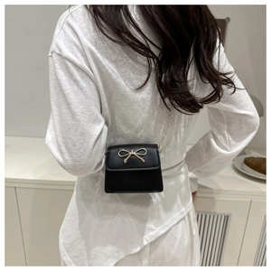 Detail showing the elegant gold bow buckle and fine chain strap of a black crossbody bag