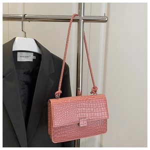 Pink crossbody bag with crocodile texture and silver buckle hanging on a metal rack