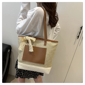 Detailed view of woven straw bucket bag with brown leather handles and lace bow detail