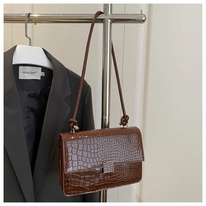 Detail of coffee brown square bag with crocodile pattern and silver metal buckle