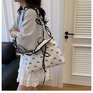 Detail of white tote bag with black bow print and ruffled shoulder strap