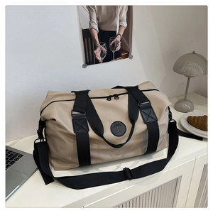 Detail of a large khaki nylon travel bag with black straps and double zippers on a desk