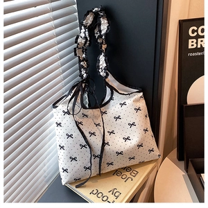 Detail of white nylon tote bag featuring black bows, dots and ruffled pleated handles