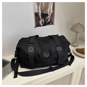 Detail of black large capacity travel bag with reinforced straps and logo on white desk