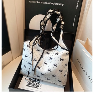 Detail of white polka dot canvas tote featuring ruffle handle and black ribbon bow accent