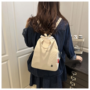 Rear view of a chic beige fabric backpack with red fashion tag worn by a female model