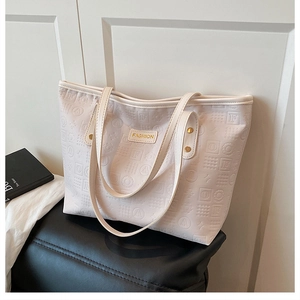 Détail d'un cabas crème avec motifs géométriques embossés et plaque dorée mode