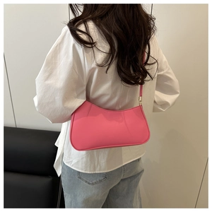 Detail of a bright pink baguette bag worn on shoulder with stylish semi-circle shape