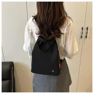 Rear view of model wearing a black trapezoid nylon backpack with metal M logo