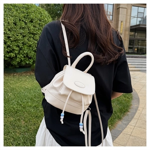 Outdoor shot of a beige mini backpack with drawstring closure and blue bead accents