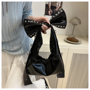 Sac à main nœud noir brillant avec rivets argentés porté par un mannequin en été